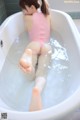 A woman in a pink bathing suit is sitting in a bathtub.