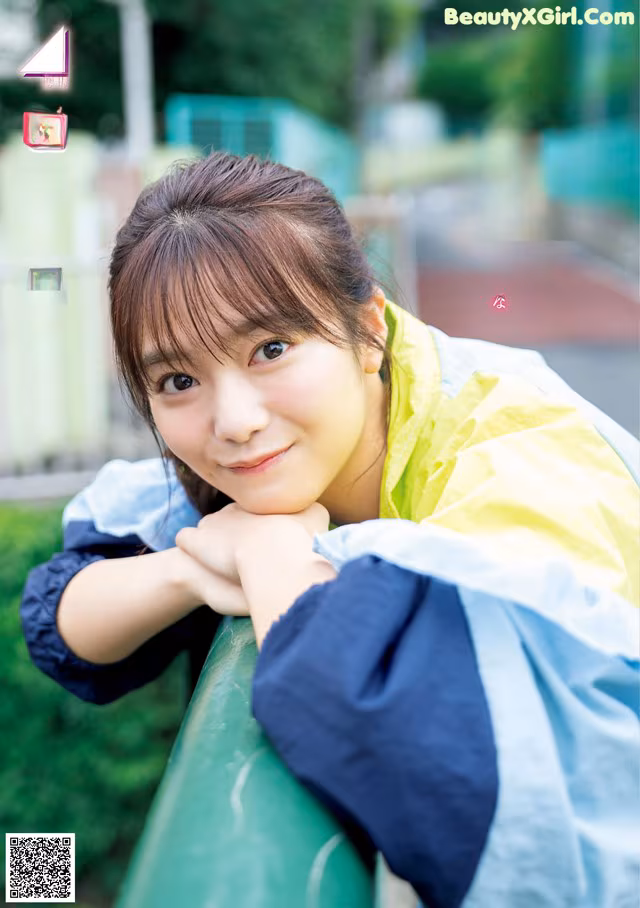 A young woman leaning against a green fence.