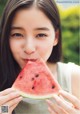 A woman holding a slice of watermelon in front of her face.