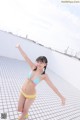 A woman in a bikini standing on a tiled floor.