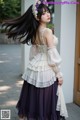 A woman with long black hair wearing a white top and purple skirt.