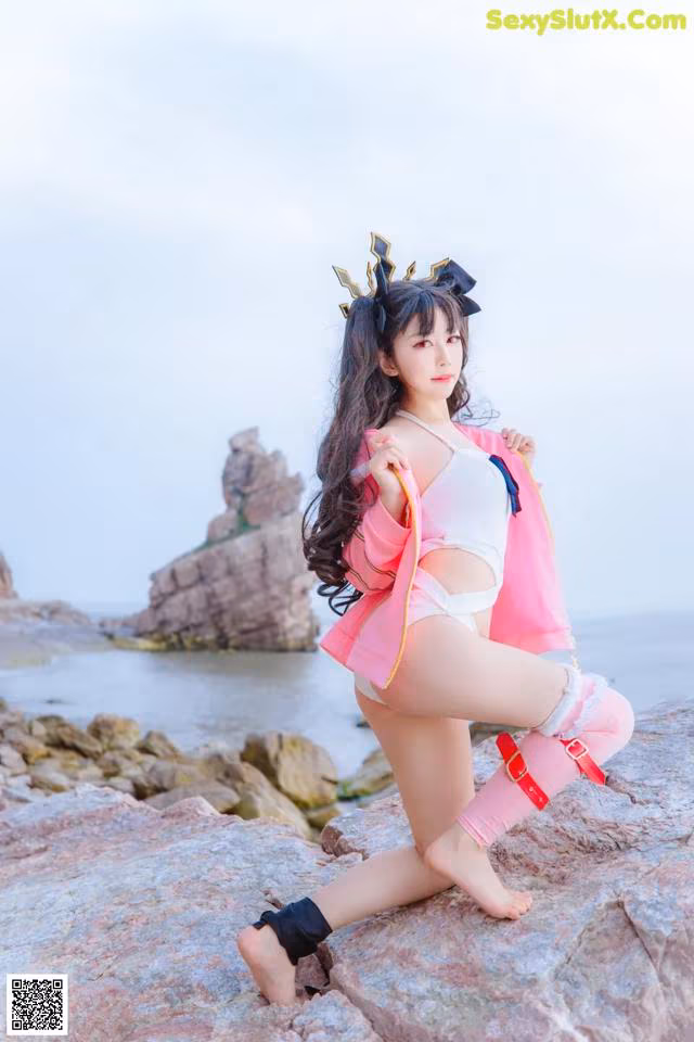 A woman in a pink and white outfit posing on a rock.