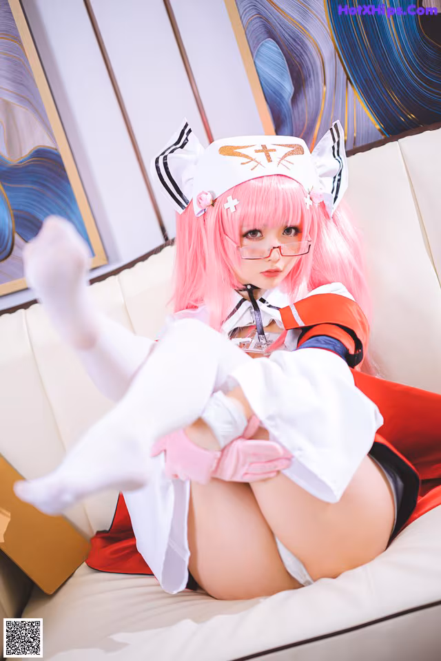 A woman with pink hair sitting on a white couch.