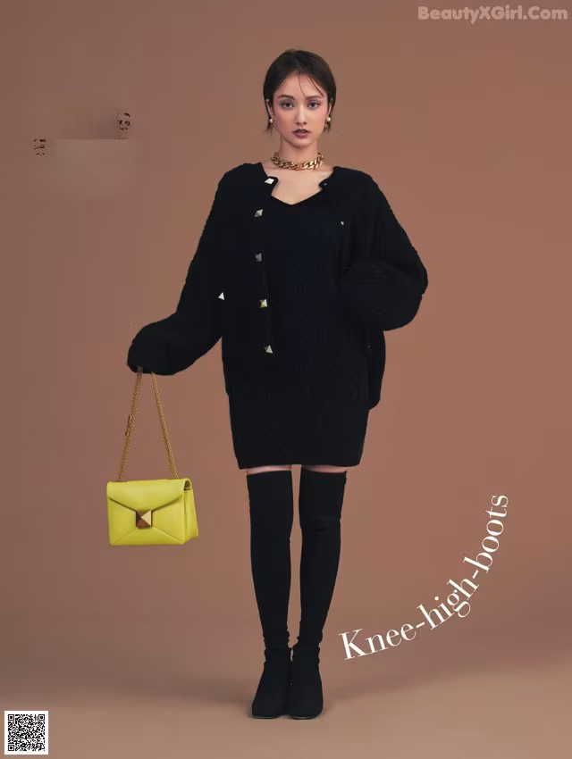 A woman in a black sweater dress and thigh high boots holding a yellow bag.