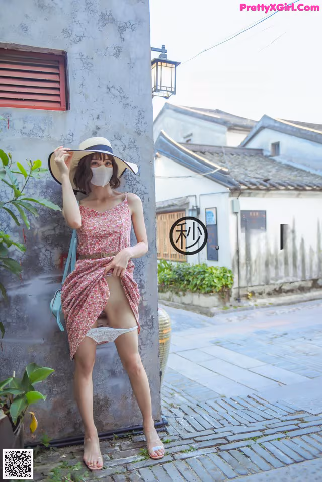 A woman wearing a hat and a face mask leaning against a wall.