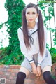 A woman in a school uniform sitting on a brick wall.