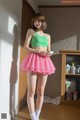 A woman in a green top and pink skirt posing for a picture.